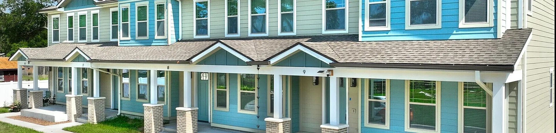 Charming townhouse complex with elegant blue facade and inviting front porches, set against a clear blue sky.
