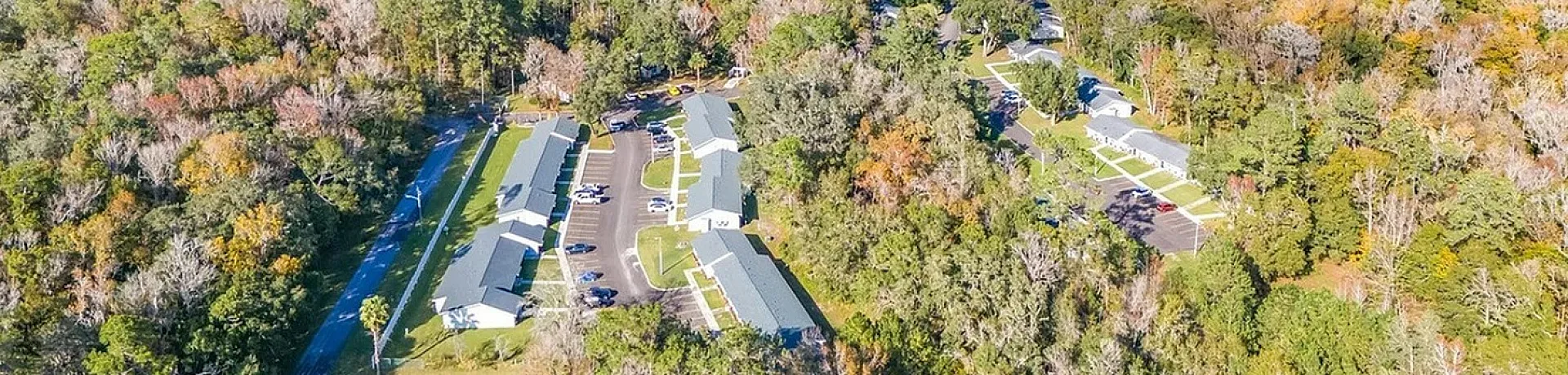Scenic aerial view of charming apartment community nestled in lush, vibrant forest landscape, basking in bright sunlight for serene living.