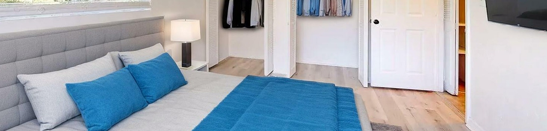 Inviting bedroom with elegant decor featuring a plush bed with blue accents, modern flat screen TV, and spacious double closets.