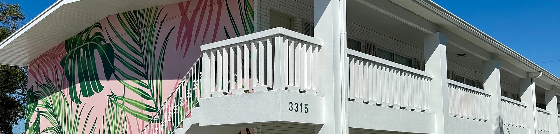 Charming apartment building with vibrant leaf-themed mural and spacious balconies, ideal for a sunny lifestyle.