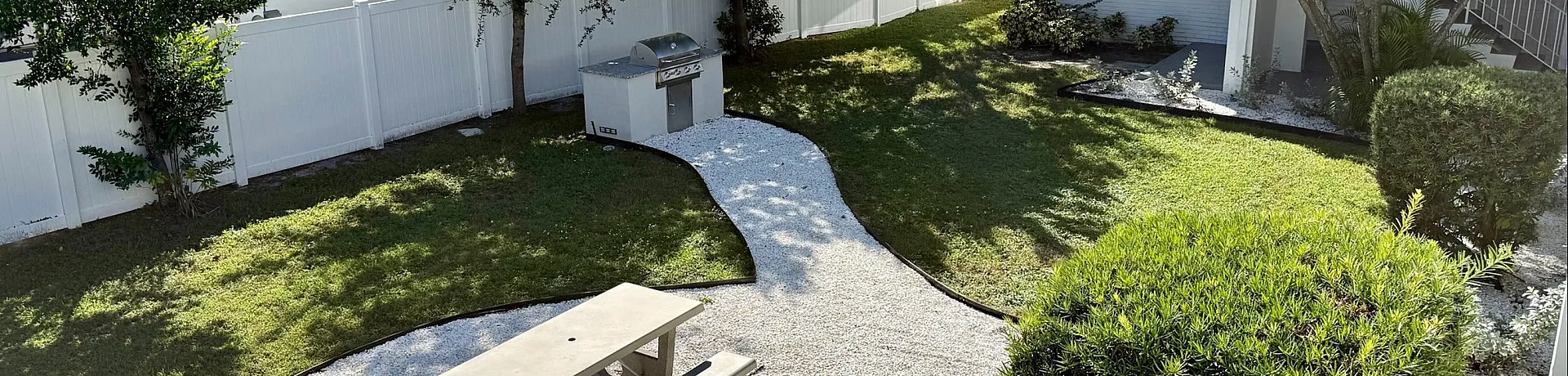 Charming outdoor space featuring a picnic area with a stone pathway, lush greenery, and a quaint apartment building in the background.