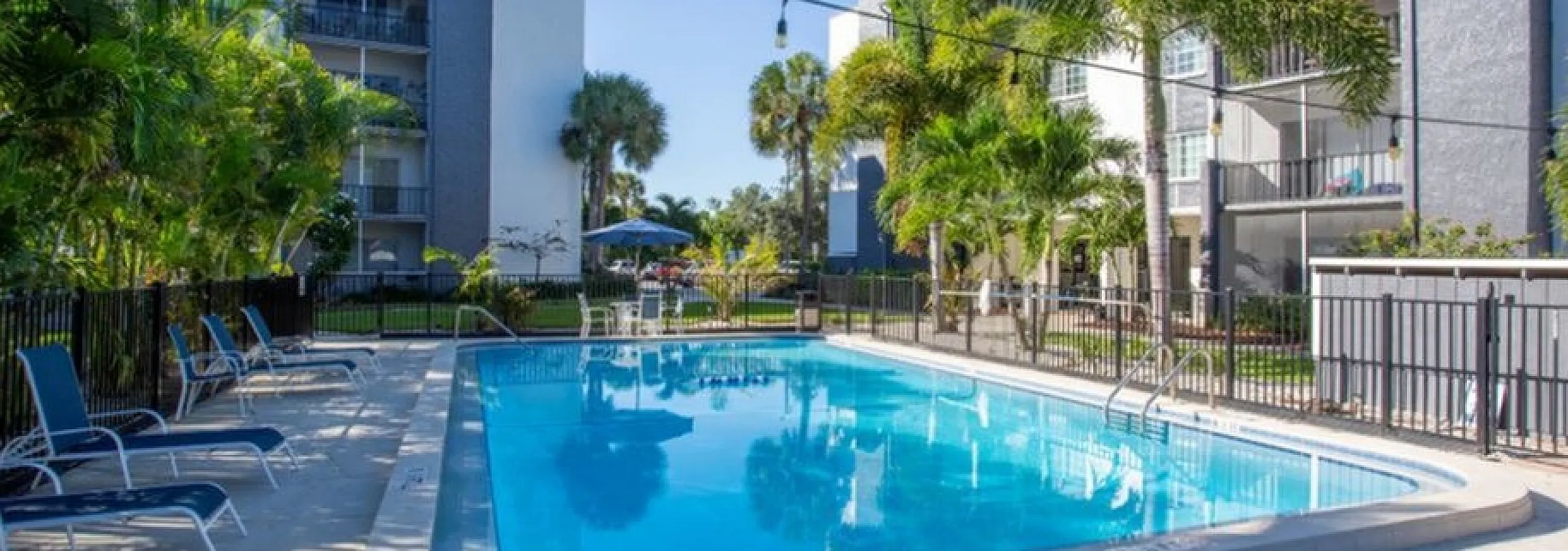 Inviting outdoor pool area surrounded by lush palm trees and modern apartment buildings, perfect for relaxation and entertainment.