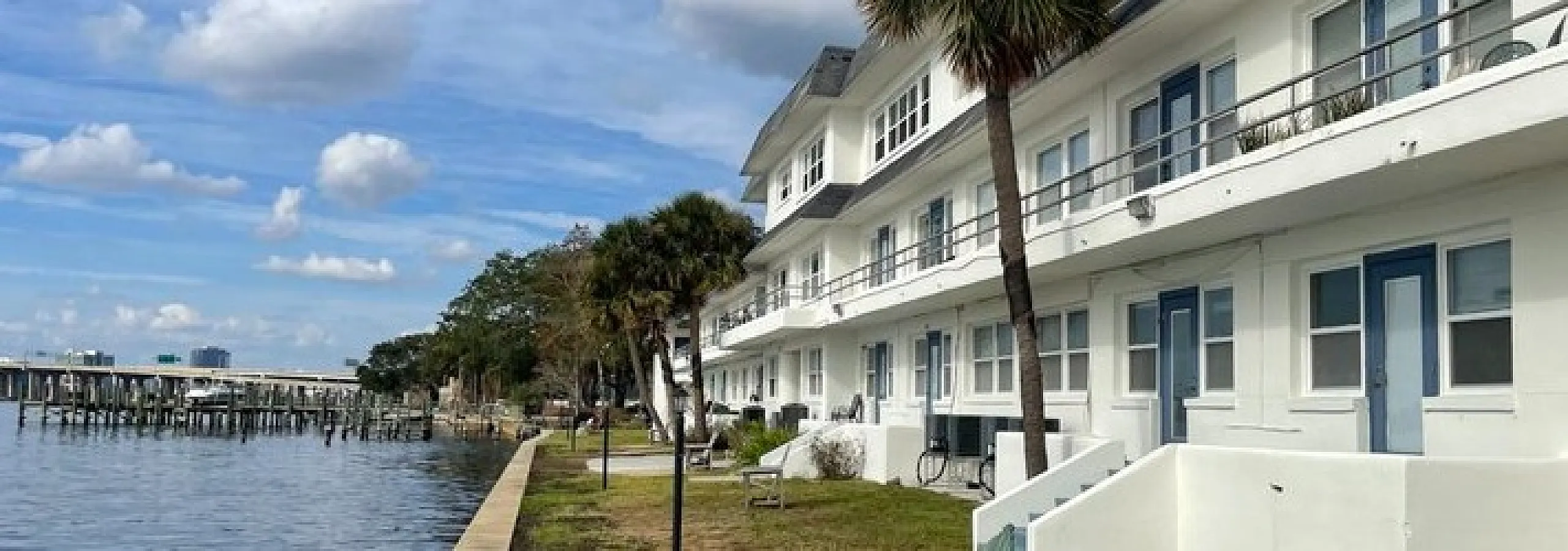 Beautiful waterfront apartment complex under a vibrant sky, offering serene views and palm trees for a relaxing lifestyle.