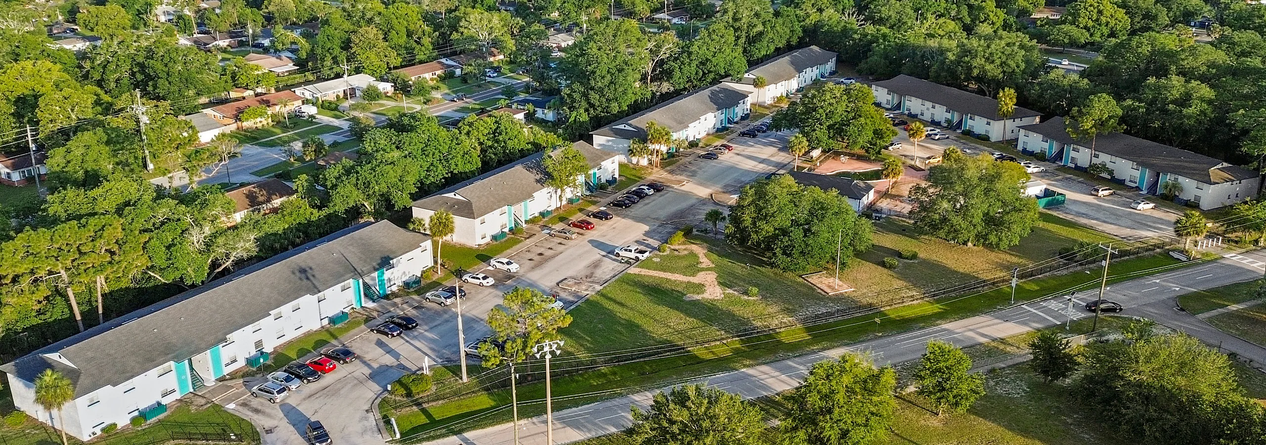 Charming aerial view of a vibrant apartment complex surrounded by lush greenery and well-maintained roads, offering a serene suburban living experience.