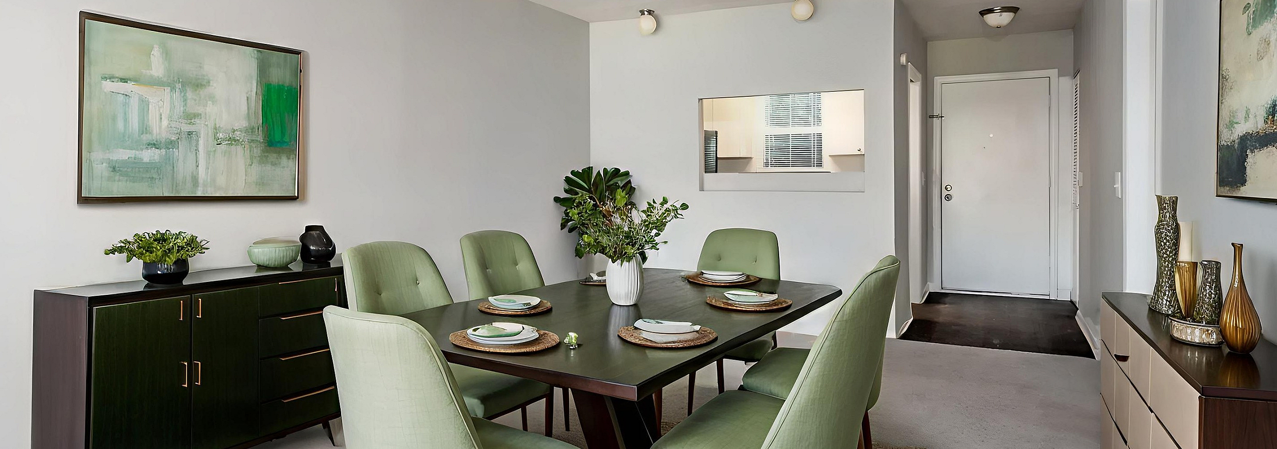 Elegant dining area featuring a modern table with six stylish green chairs, flanked by chic artwork and a sleek sideboard for a welcoming ambiance.