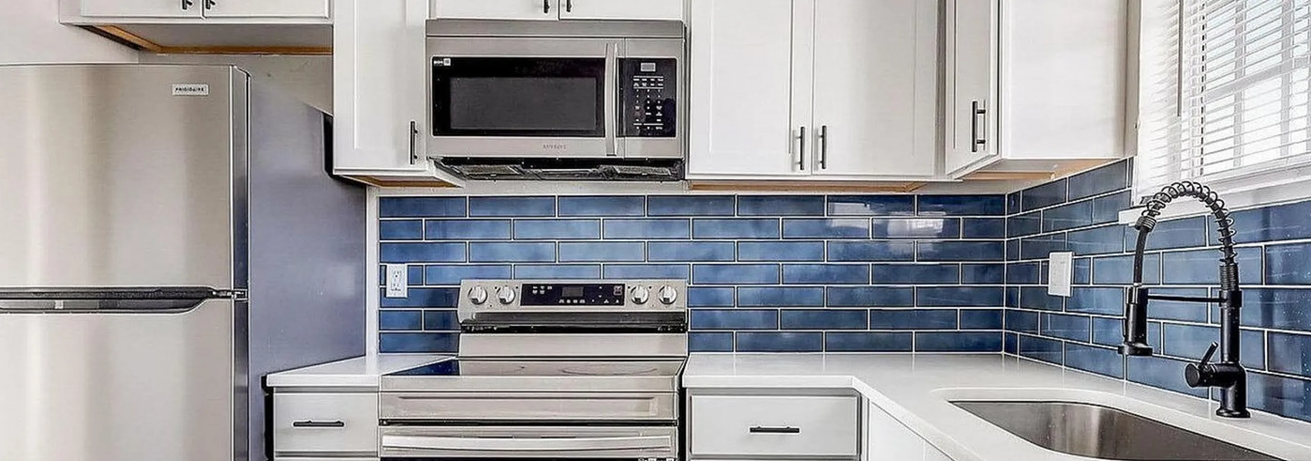 Modern kitchen with sleek white cabinetry, stainless steel appliances, and elegant blue subway tile backsplash.