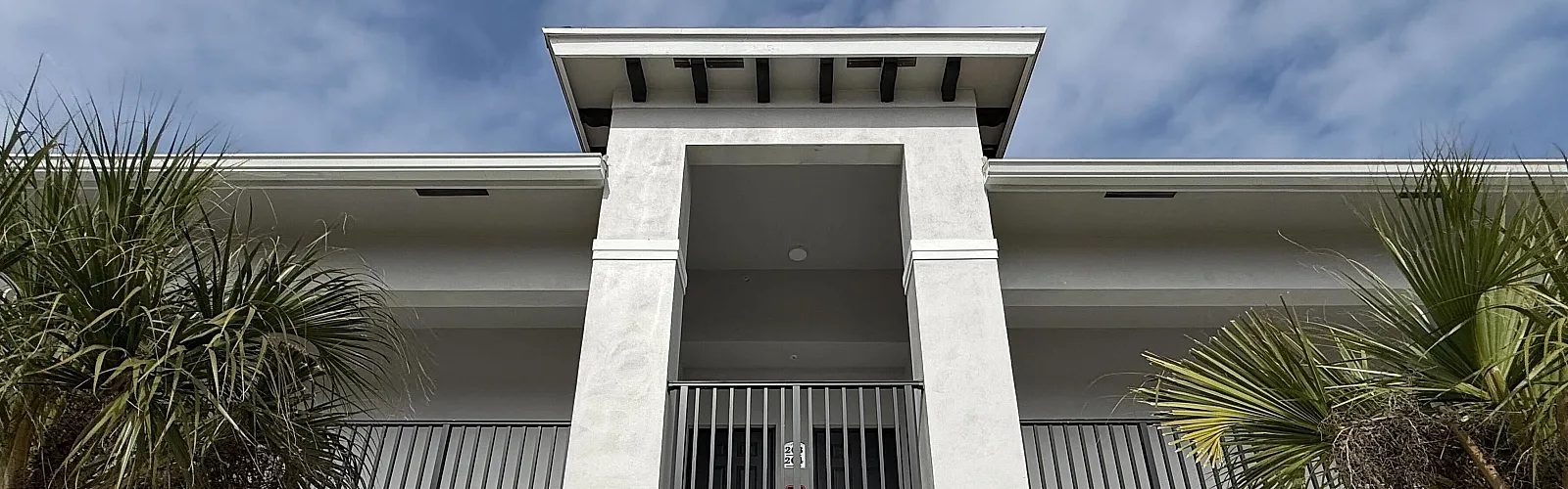 Charming two-story building with modern architecture, surrounded by lush tropical landscaping under a bright, clear sky.