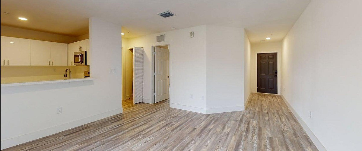 Modern apartment interior with elegant wood flooring, a bright kitchen with white cabinets, and a spacious hallway.