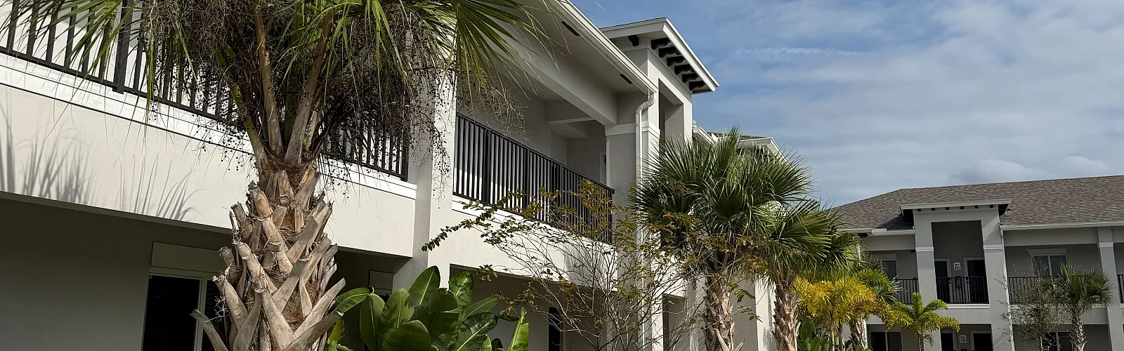 Charming apartment with modern exterior, lush tropical landscaping, and inviting walkways under a blue sky.
