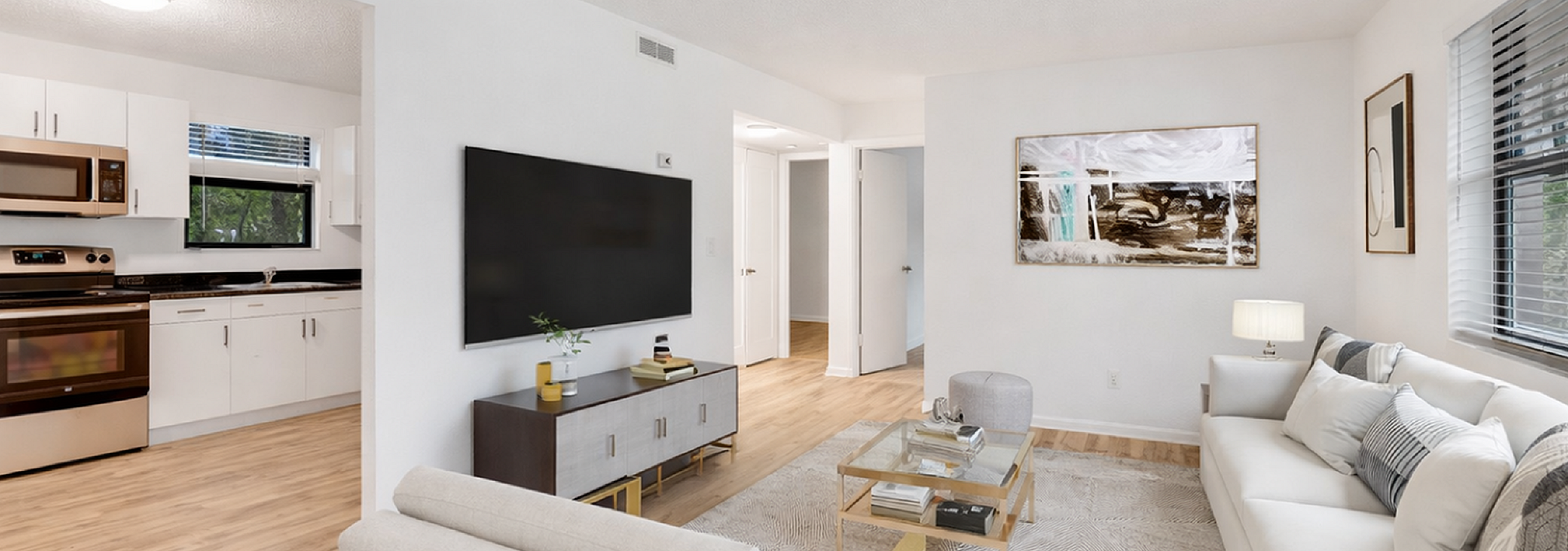 Modern open-plan living area with a cozy sofa, large flat-screen TV, and sleek kitchen in the background.