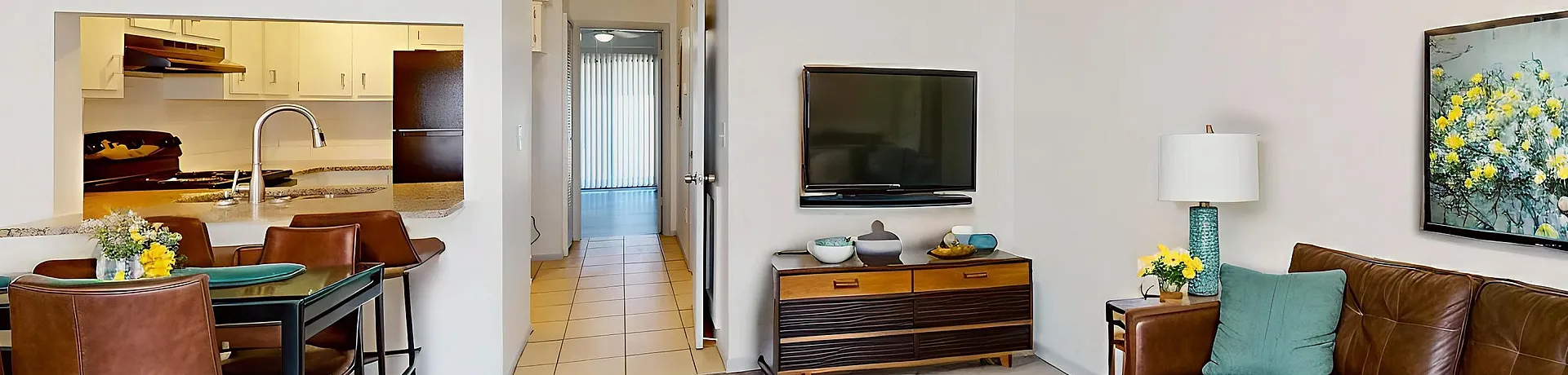 Modern apartment living room with elegant brown leather sofa, vibrant yellow flower decor, sleek TV setup, and view into a stylish open kitchen with dining area.