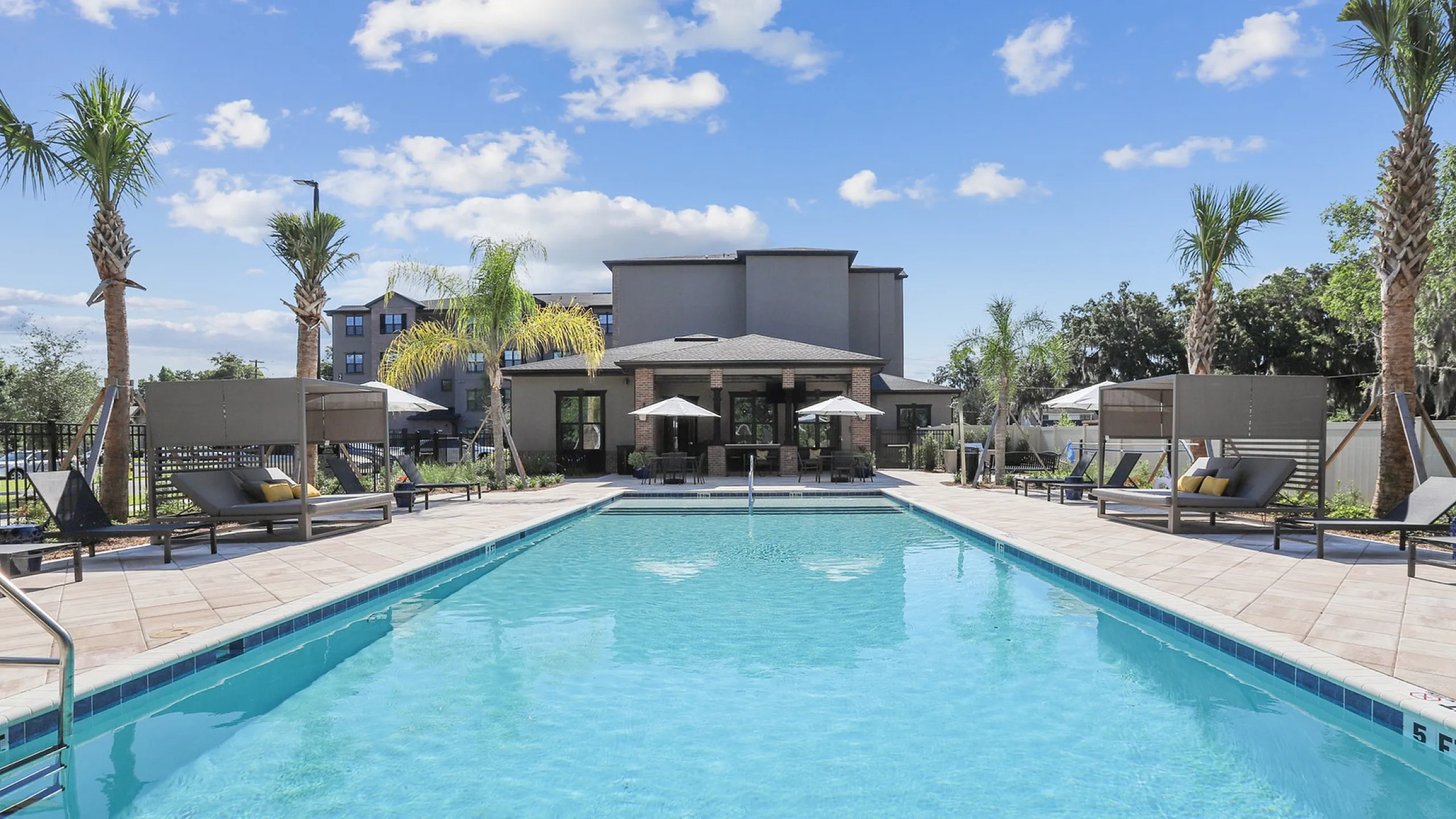 Luxurious apartment community featuring a sparkling outdoor pool with elegant poolside loungers and palm trees.