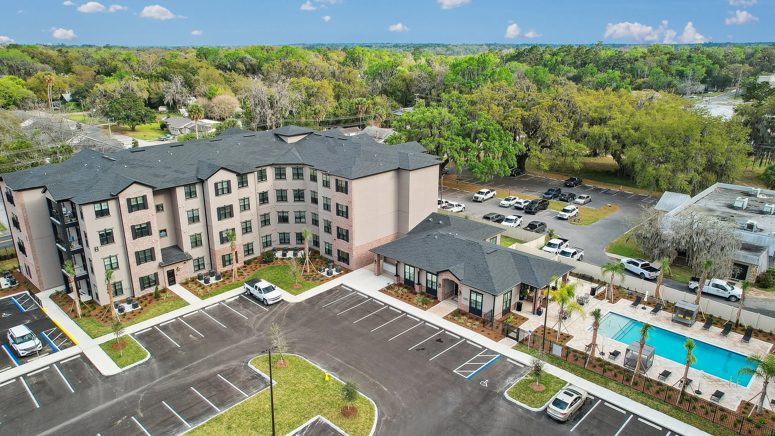 Modern apartment complex aerial view featuring lush greenery, spacious parking, and a luxurious swimming pool.