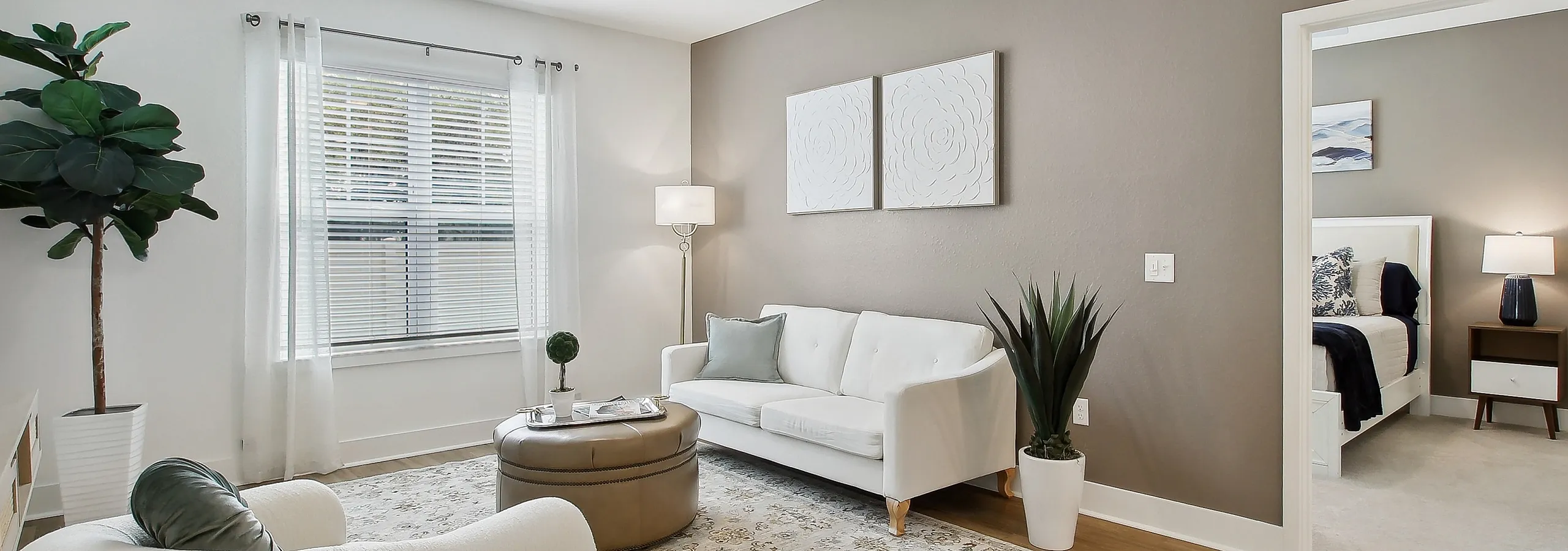 Bright and modern living room featuring cozy white furniture, natural light from large windows, and a stylish open connection to the bedroom.