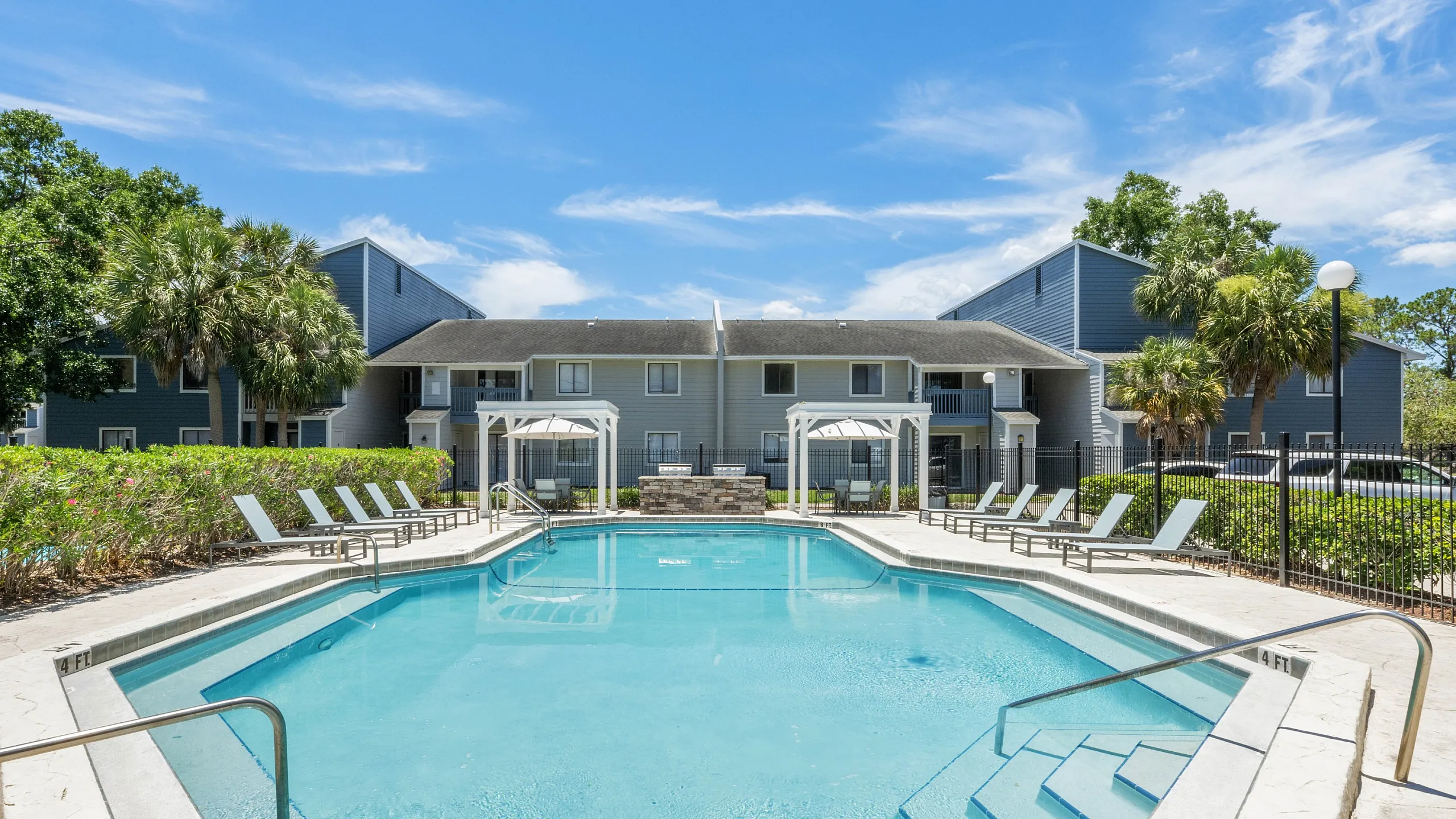 Inviting apartment complex featuring a stunning outdoor pool with lounge chairs, surrounded by lush greenery and modern architecture.