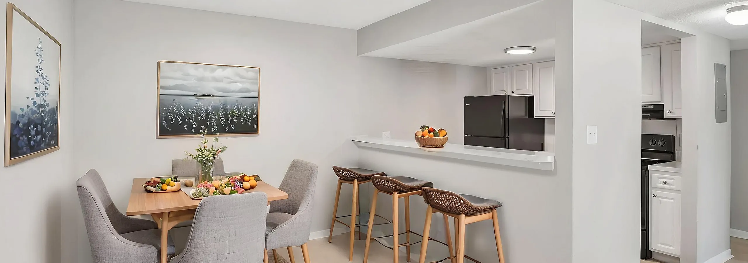 Modern dining area with elegant wooden table and plush gray chairs, adjacent to a chic kitchen with a stylish breakfast bar and sleek appliances.