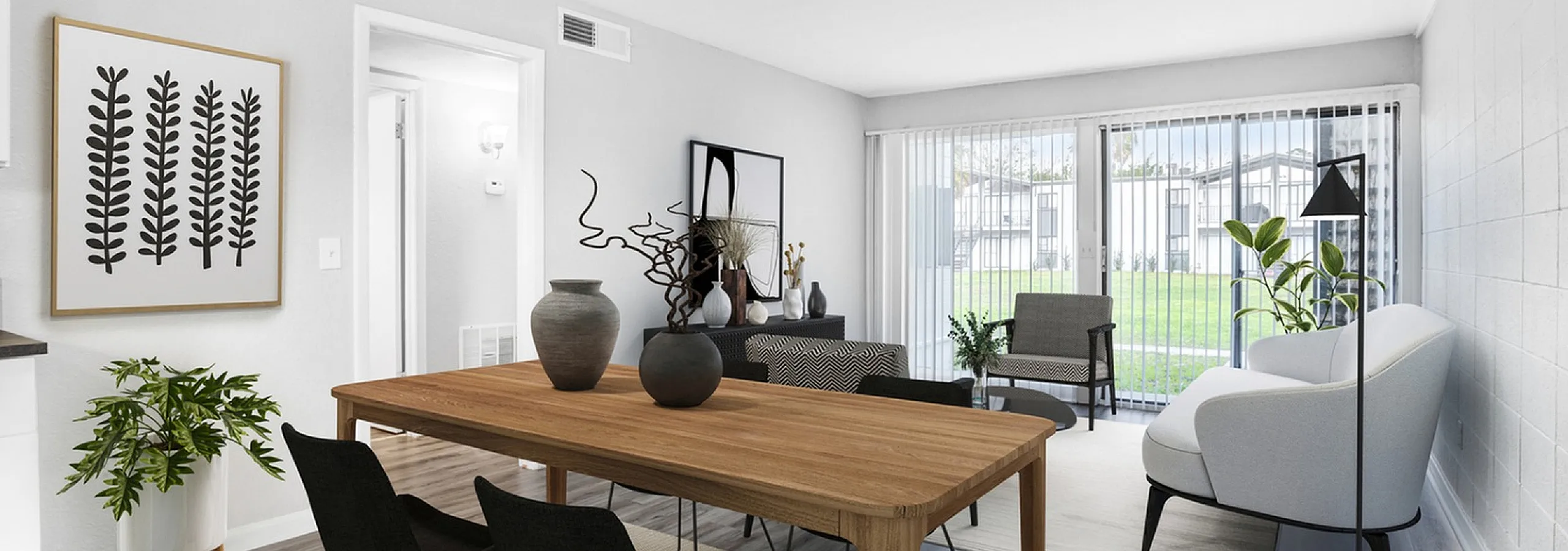 Bright and modern apartment living area featuring a stylish dining table, comfortable seating, and floor-to-ceiling windows with garden views.