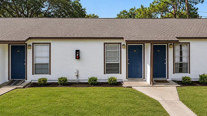 Charming single-story apartment with blue doors and manicured lawn in a peaceful setting.