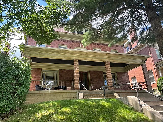 Inviting brick apartment building with a welcoming front porch and lush greenery.