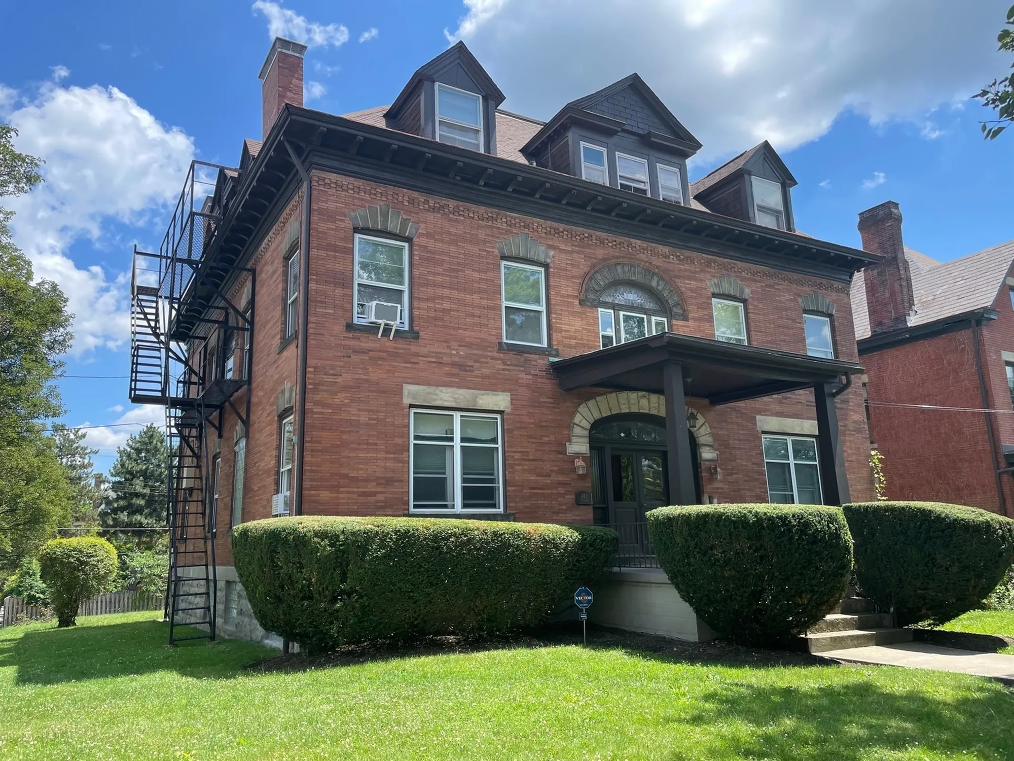 Elegant historic brick house with multiple floors, manicured hedges, and a scenic backdrop of blue skies.