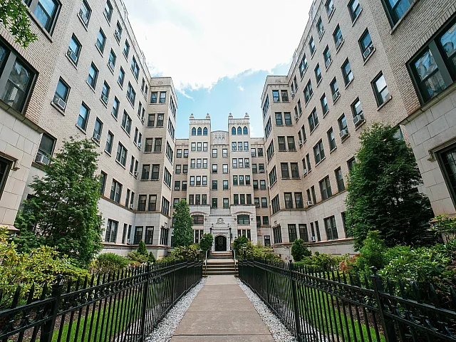 Elegant brick apartment complex with lush landscaping and a charming entrance pathway.