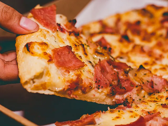 Close-up of a deliciously cheesy slice of pizza topped with crispy bacon, being pulled from a box. Mouthwatering and savory, perfect for pizza lovers.