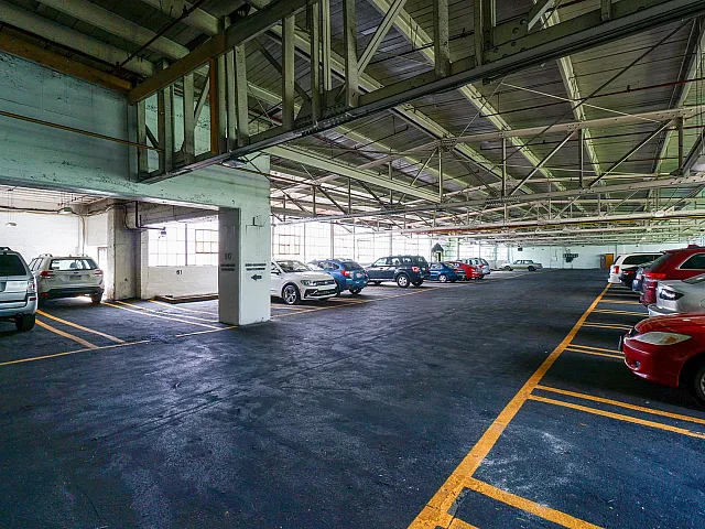 Spacious, well-lit indoor parking garage with multiple vehicles parked neatly in marked spots, featuring high ceilings and industrial-style architecture.