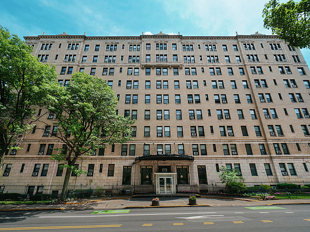 Charming urban apartment building with classic architecture, nestled amidst lush trees and clear blue skies.