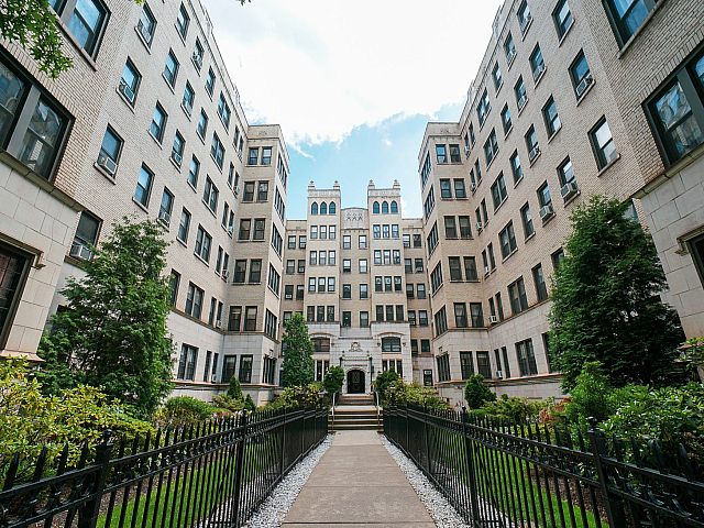 Elegant apartment building facade with classic architecture, lush greenery, and inviting pathway leading to a grand entrance.