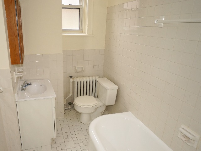 LeBaron unit bathroom, with cream walls and white tile flooring. Full bathtub, toilet, and sink.