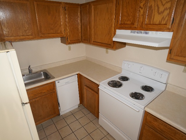 Artena unit showing kitchen with cream colored walls, and tan colored tile flooring. Kitchen equipped with wooden cabinets, refrigerator, dishwasher, stove, oven, and sink.