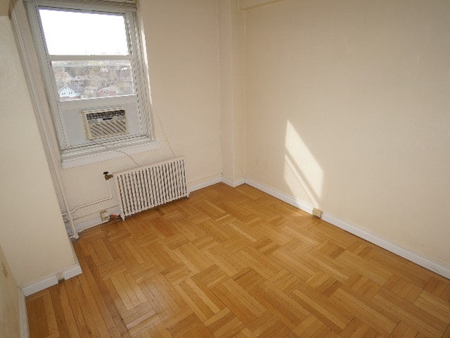 Artena unit showing bedroom with window, cream colored walls, and hardwood flooring.