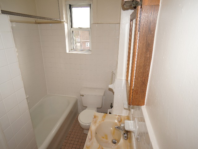 Artena unit showing bathroom with cream colored and white tile walls, tan colored tile flooring, white bathtub, toilet, and tan stone colored sink.