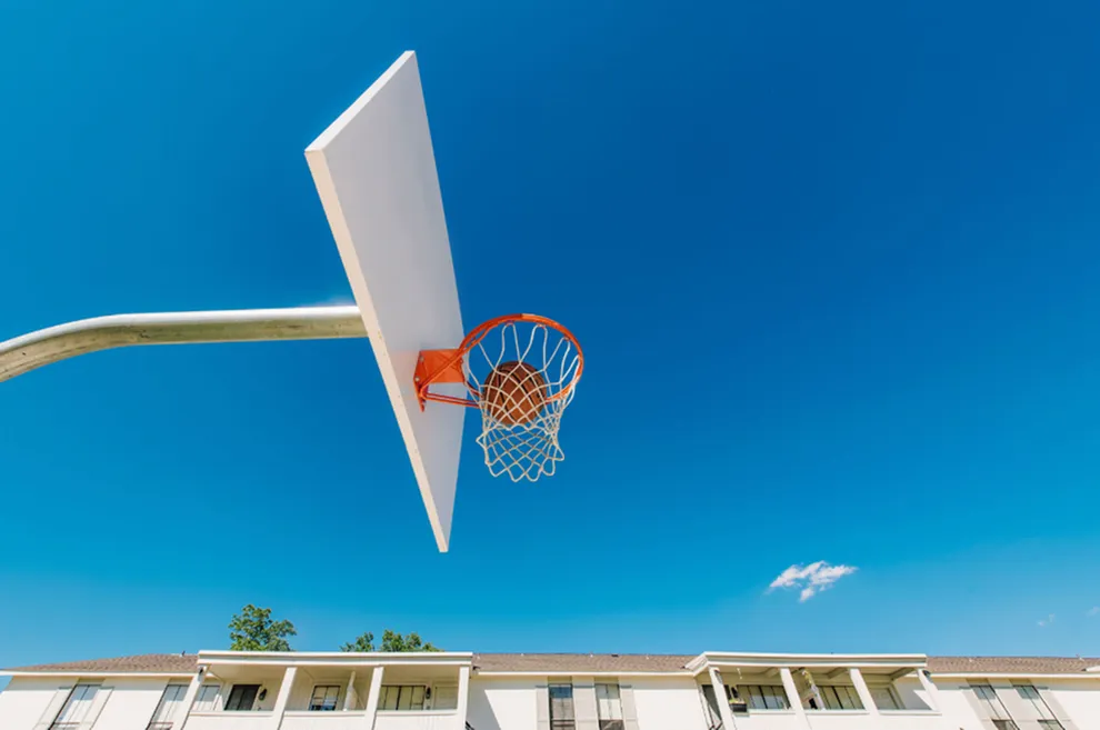 Vibrant outdoor basketball hoop against a clear blue sky, with apartment buildings in the background.