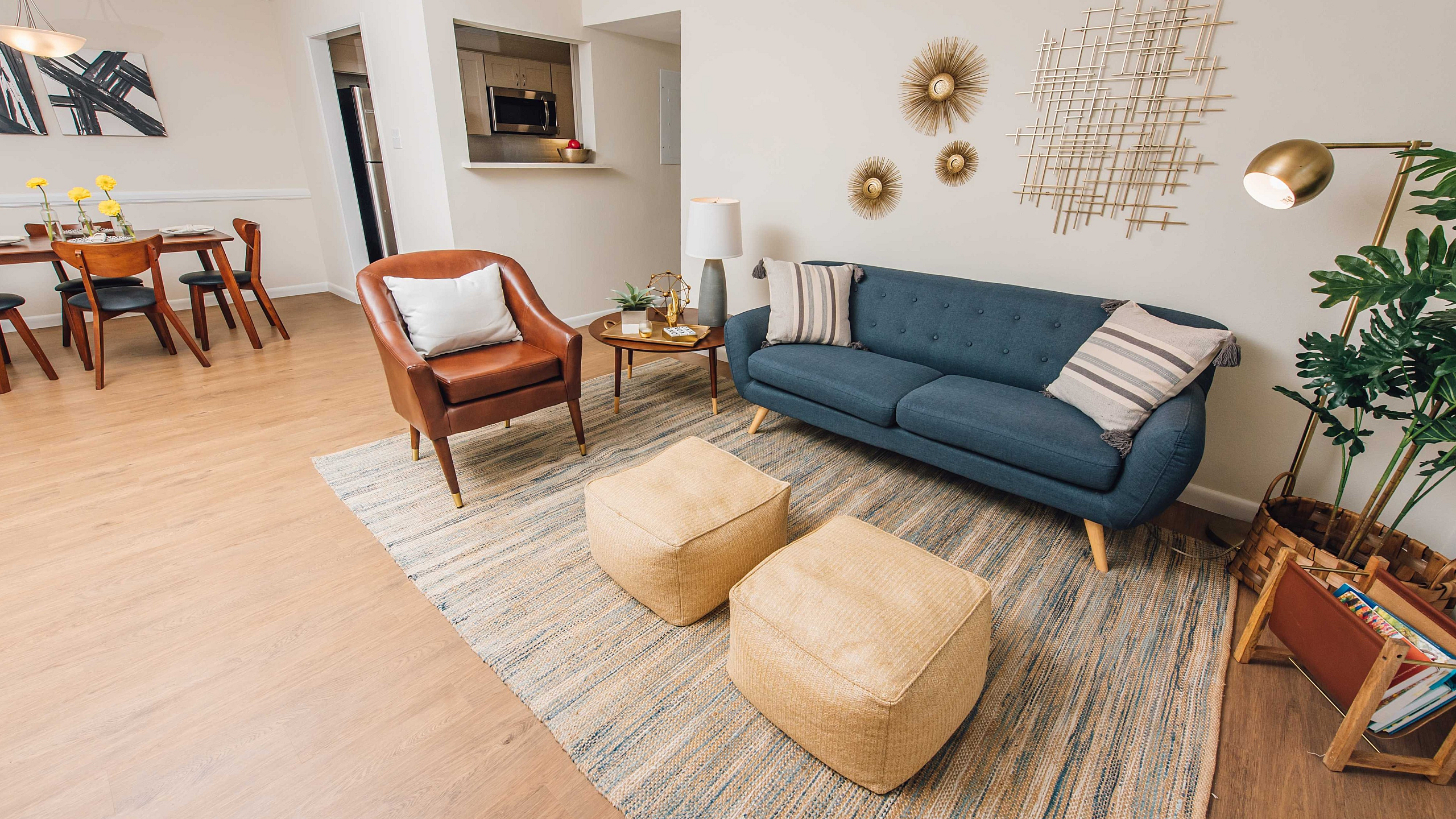 Bright, stylish living room with modern decor, featuring a comfortable blue sofa, chic leather chair, elegant dining area, and open-access kitchen.