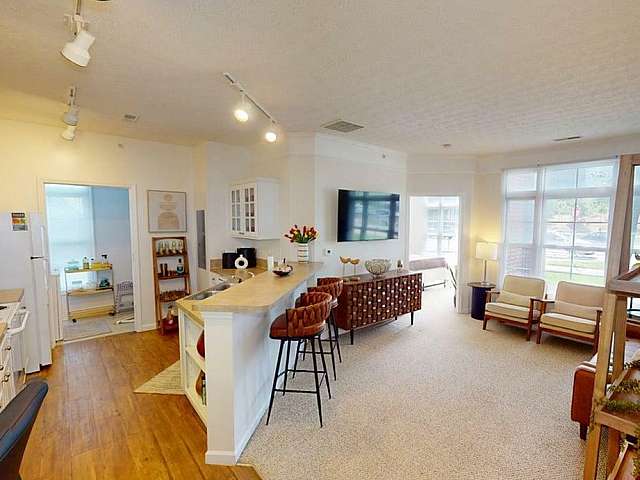 Inviting open-plan apartment featuring a modern kitchen with bar seating, cozy living area with elegant decor, and large windows allowing natural light to flood in.