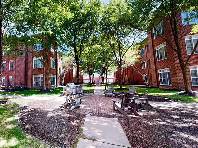 Charming brick apartment complex surrounded by lush greenery and peaceful outdoor seating area.