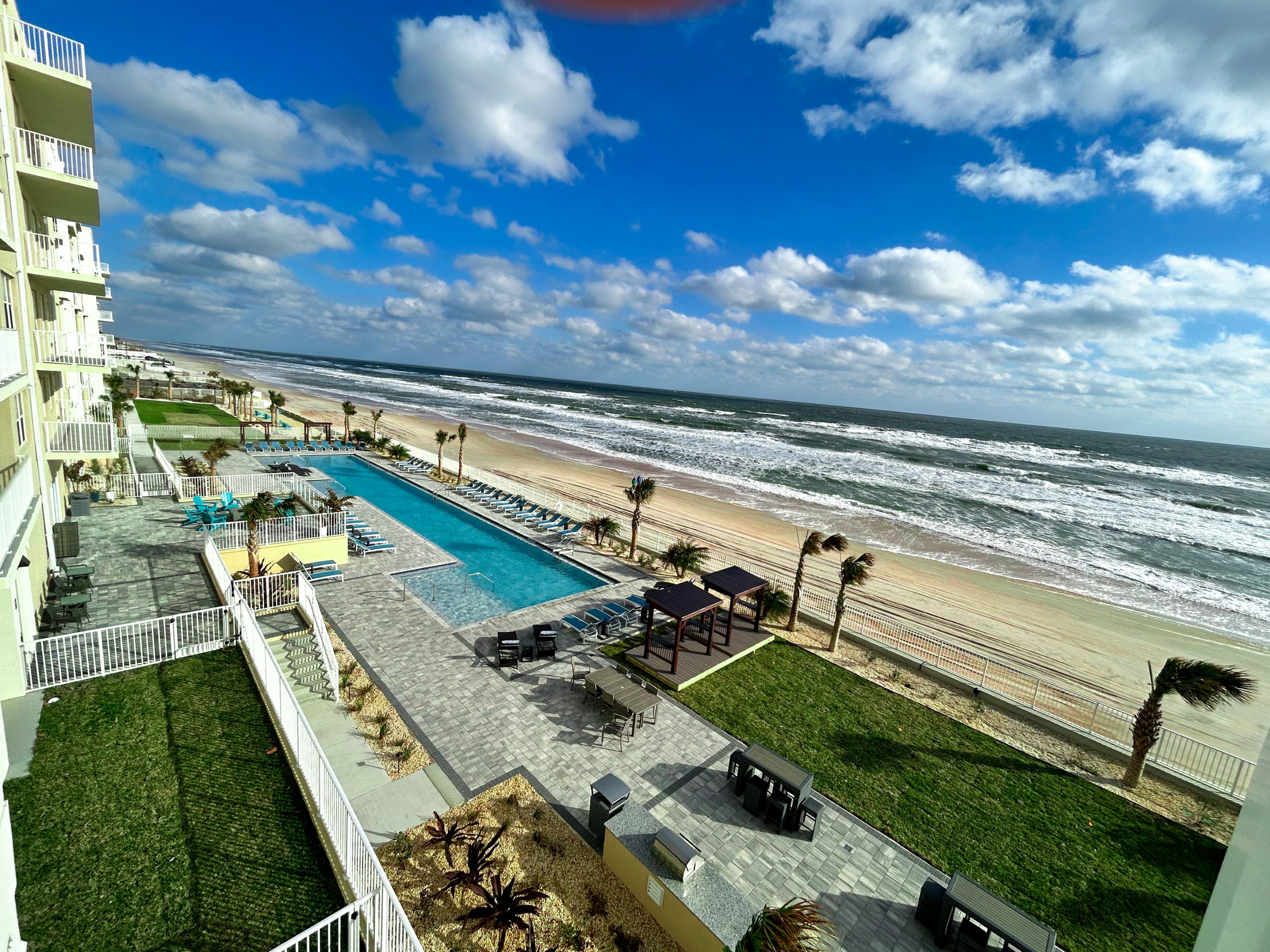Luxurious beachfront view from apartment showcasing a pristine pool, lush gardens, and serene ocean backdrop with vibrant skies.
