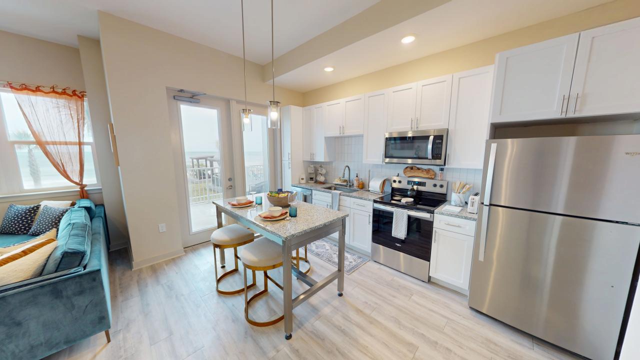 Modern kitchen with stainless steel appliances, a sleek island with stylish seating, and a cozy living area with a view of the balcony.