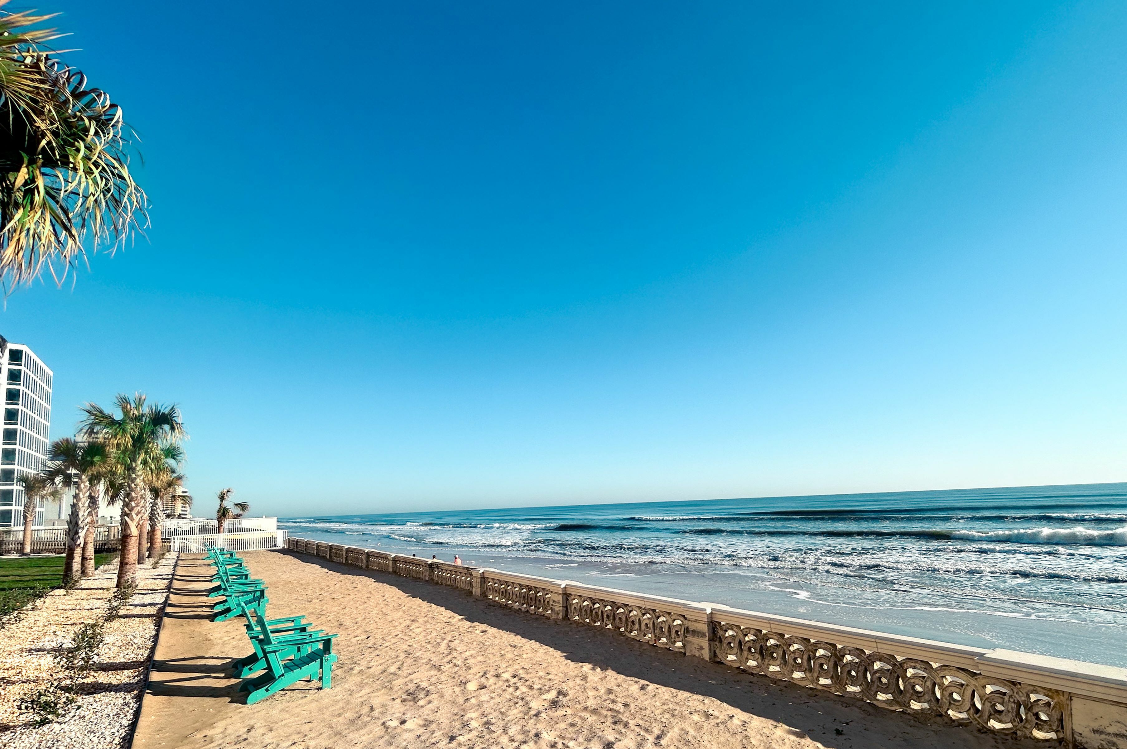 Breathtaking oceanfront view with turquoise chairs on a sandy beach under clear blue skies, perfect for relaxing by the waves.