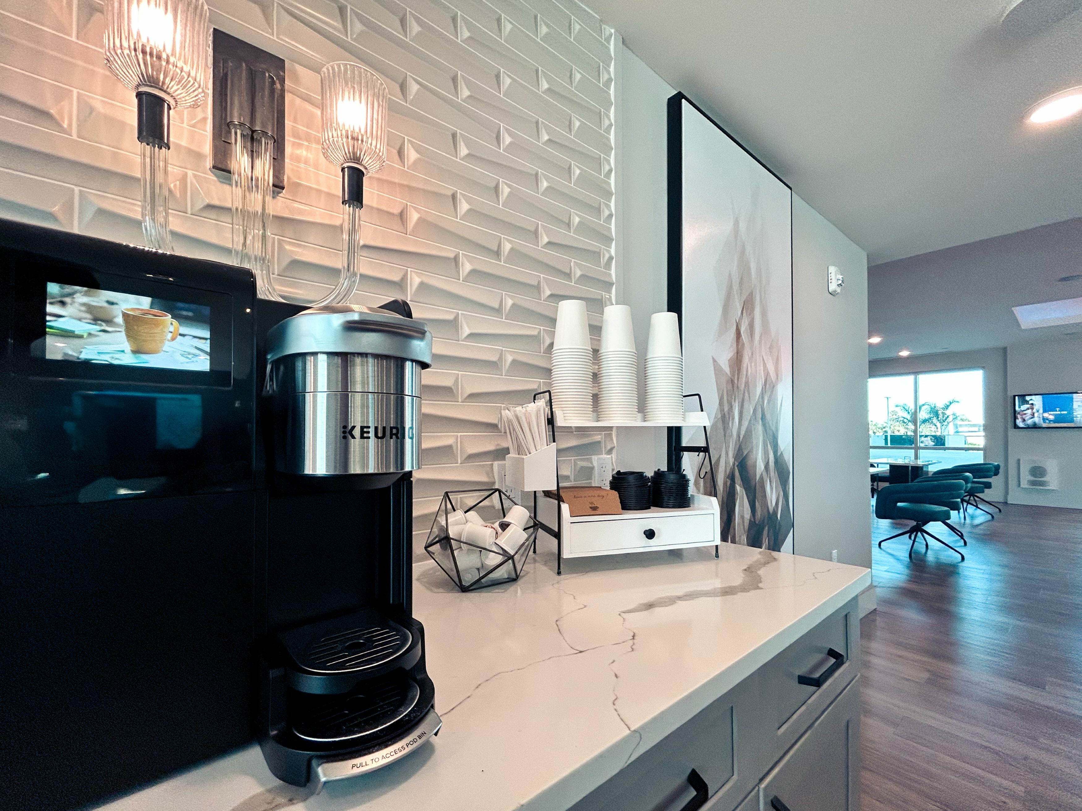 Chic apartment kitchen corner with modern coffee station, elegant lighting, and bright open living space in the background.