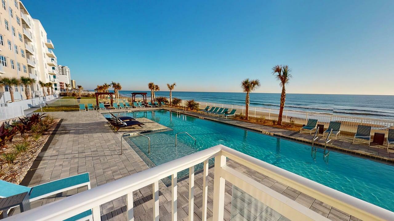 Luxurious beachfront apartment view featuring a sparkling pool and palm-lined oceanfront, perfect for a serene coastal lifestyle.