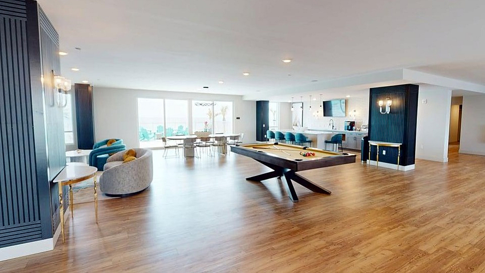 Spacious and modern entertainment lounge with sleek wood flooring, a stylish billiards table, and vibrant seating areas.