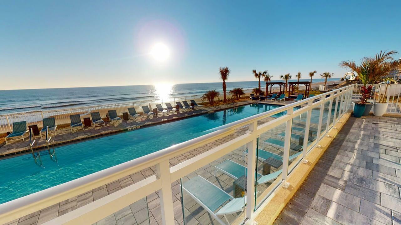 Stunning beachfront apartment view with sunlit pool, ocean waves, and inviting lounge chairs for ultimate relaxation.