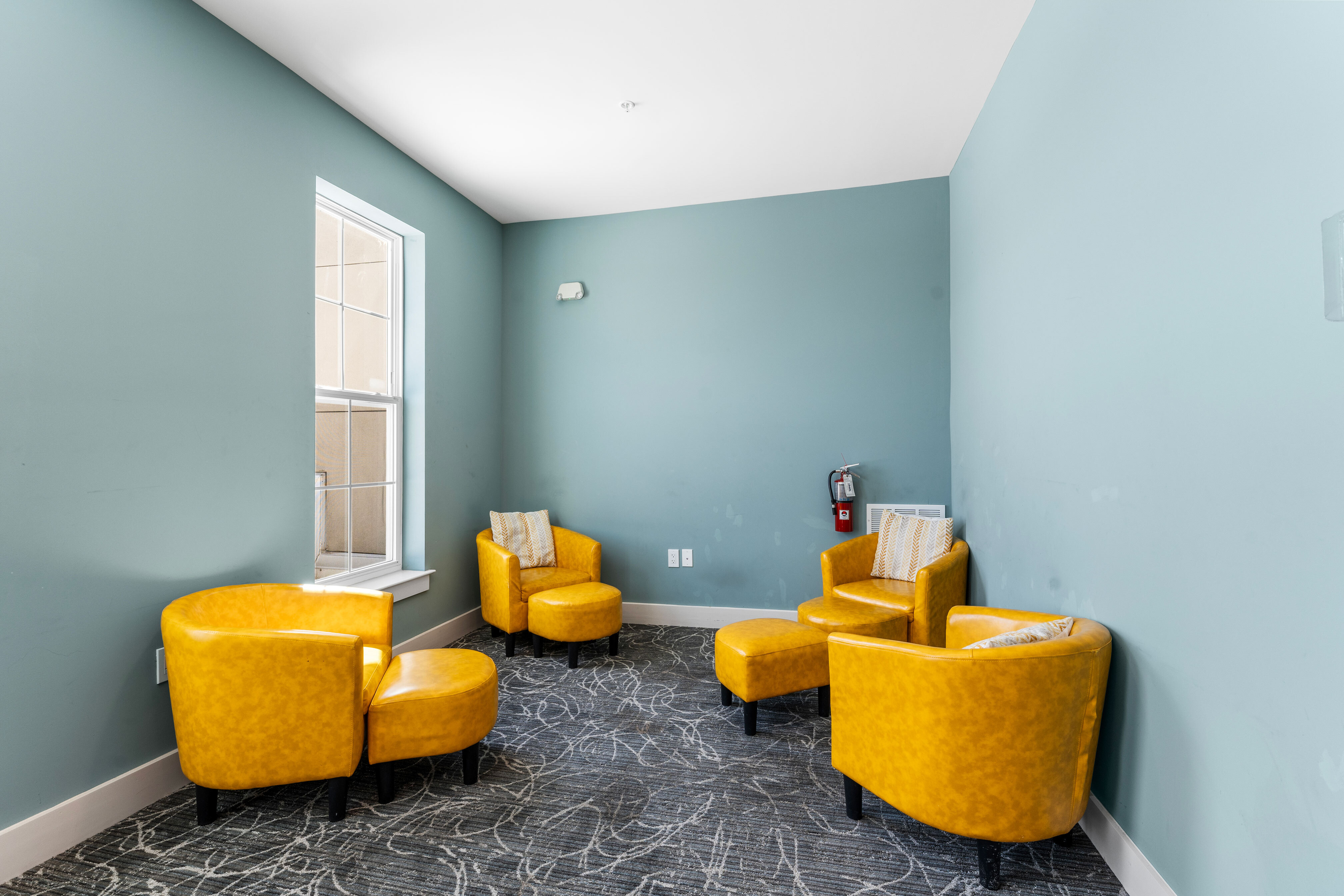 Inviting corner lounge with vibrant yellow chairs against a soothing teal wall, perfect for relaxation.