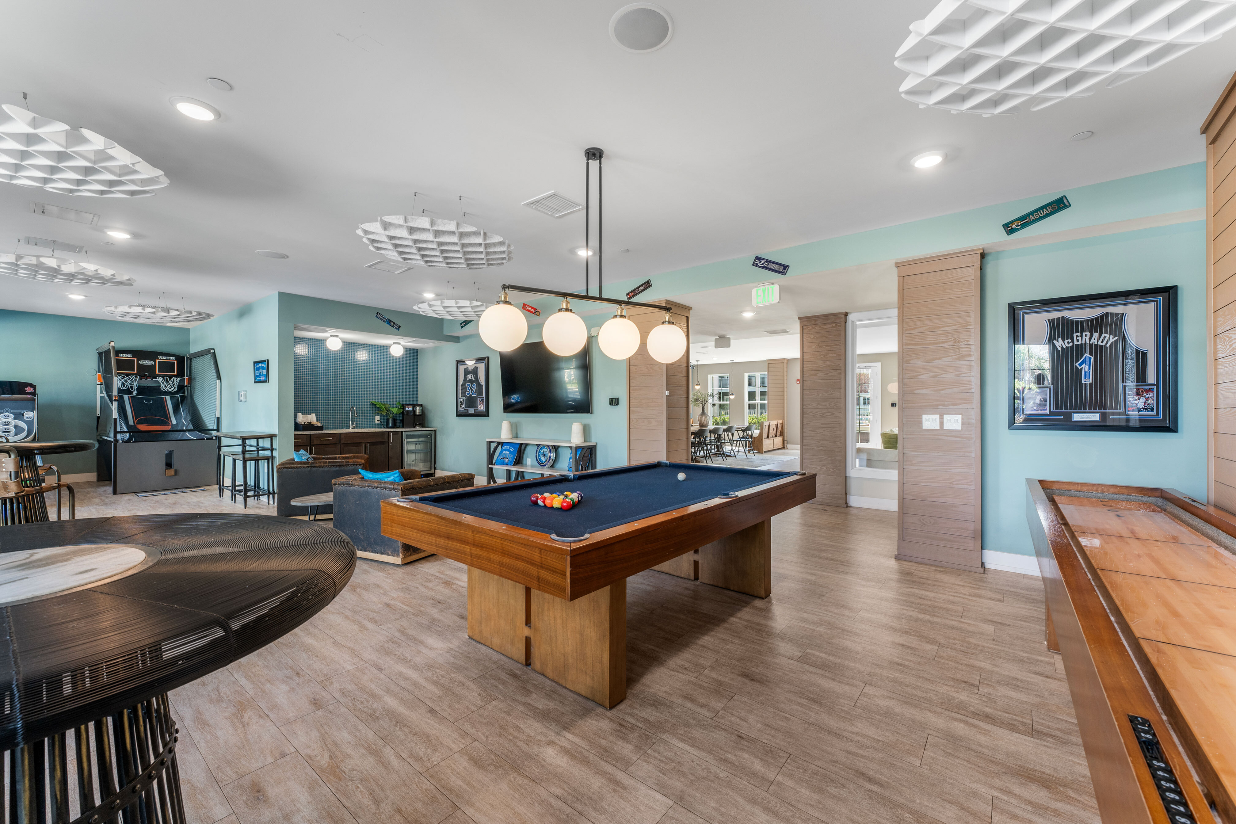 Vibrant entertainment area featuring a sleek pool table, basketball arcade game, and cozy seating under stylish lighting.