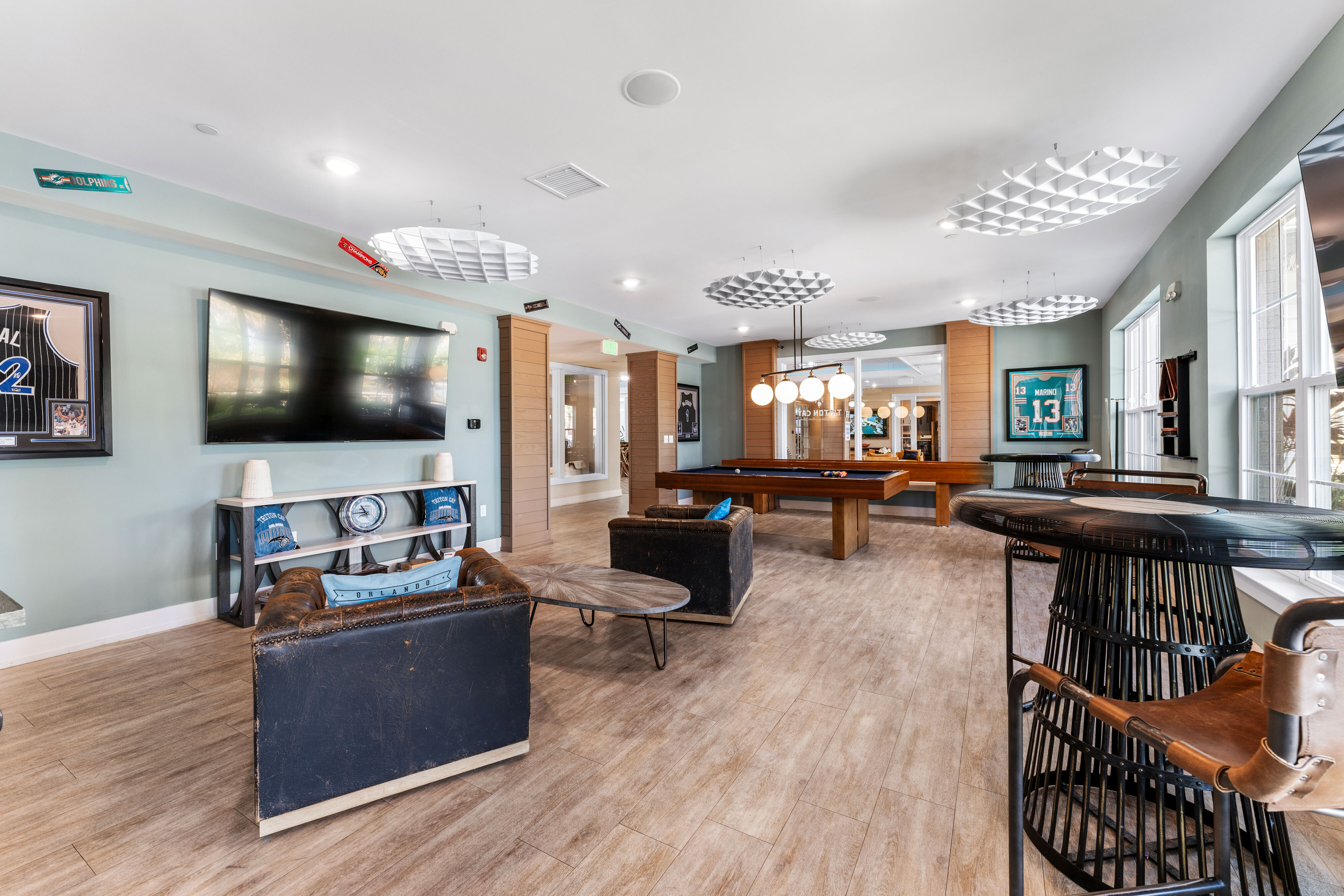 Chic modern game room with stylish decor featuring a large TV, comfortable seating, and a pool table under elegant lighting.