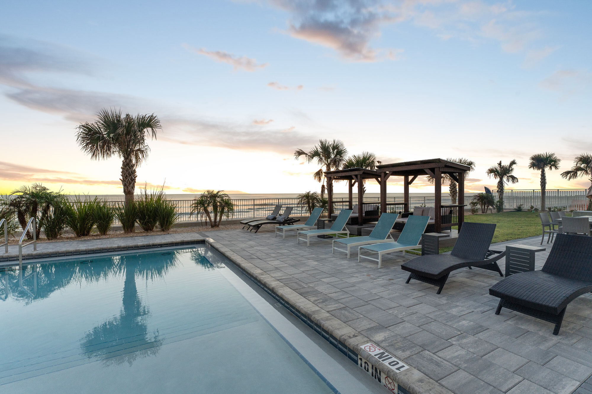 Luxurious outdoor pool area with stylish lounge chairs, elegant pergolas, and scenic ocean views at sunset.