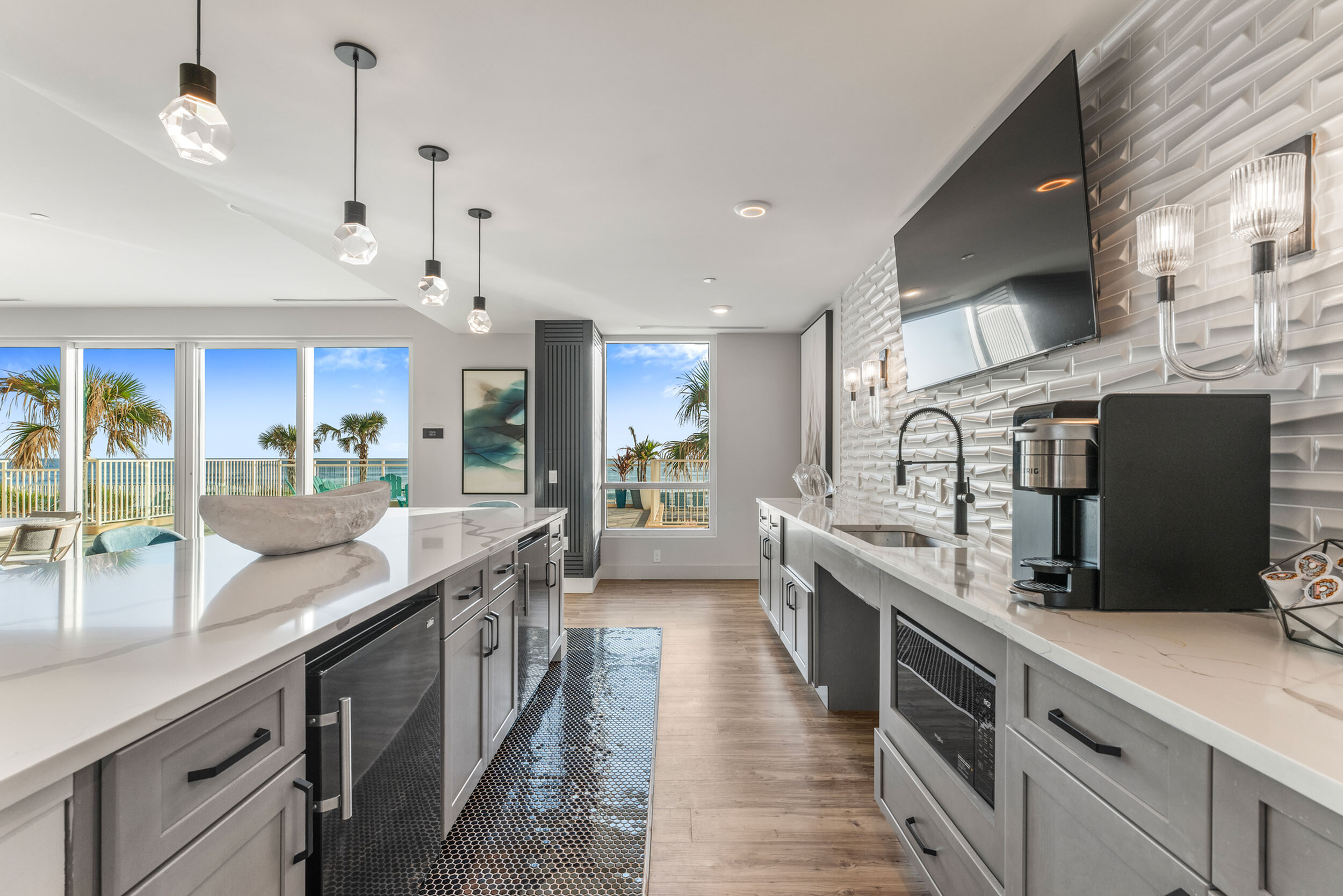 Luxury oceanfront kitchen with sleek modern design, featuring large windows, elegant pendant lighting, and stunning palm tree views.
