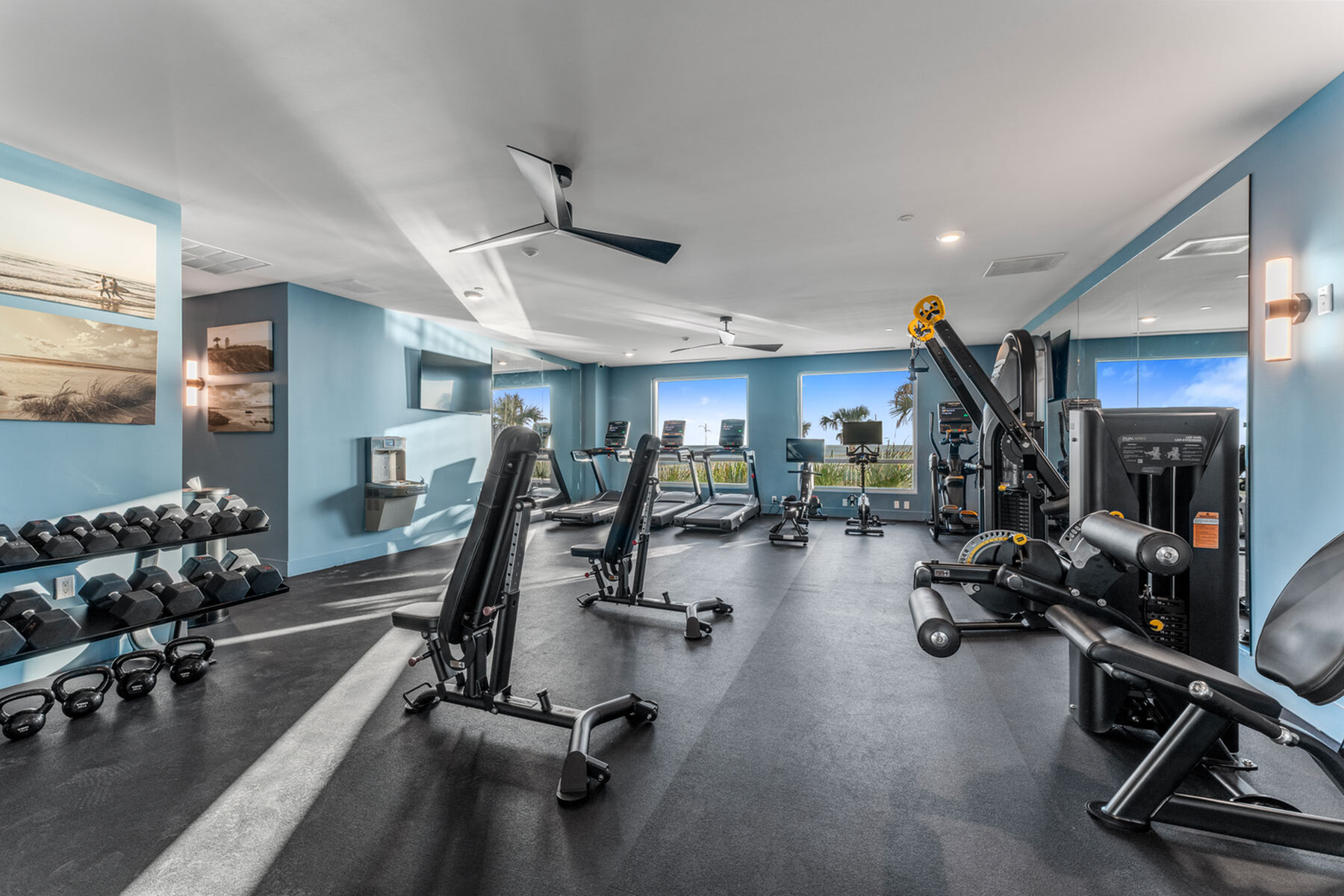 Modern fitness center with state-of-the-art gym equipment, blue walls, and large windows offering scenic views.